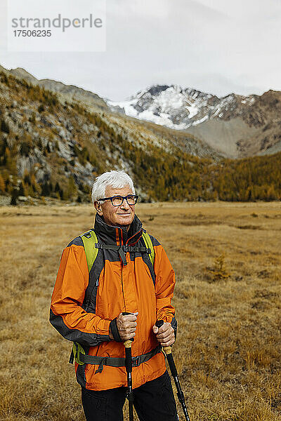 Lächelnder älterer Tourist mit Wanderstöcken  der auf die Rhätischen Alpen in Italien blickt