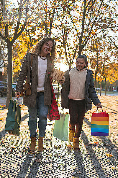 Lächelnde Mutter und Tochter mit Einkaufstüten gehen auf Fußweg