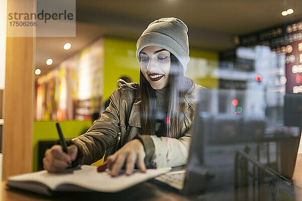 Frau schreibt Tagebuch im Café  gesehen durch Glas