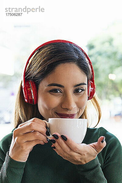 Lächelnde Frau mit kabellosen Kopfhörern und Kaffeetasse im Café