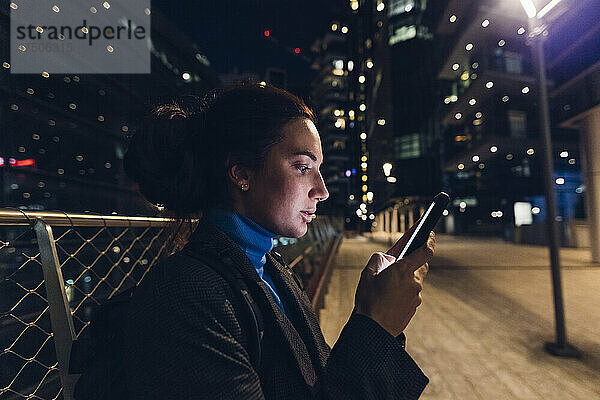 Berufstätige Frau benutzt nachts ihr Smartphone in der Stadt