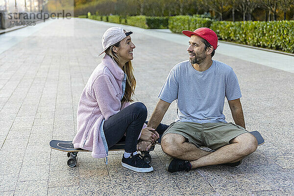 Paar redet miteinander und sitzt auf dem Skateboard am Fußweg