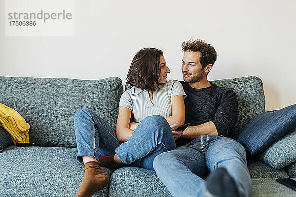 Lächelndes Paar  das einander anschaut  während es auf dem Sofa sitzt