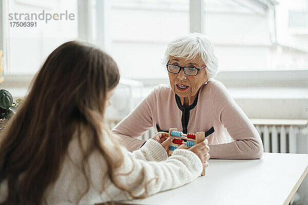 Ältere Frau spricht mit Mädchen mit Abakus am Tisch