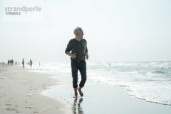 Älterer Mann blickt aufs Meer und geht am Strand spazieren