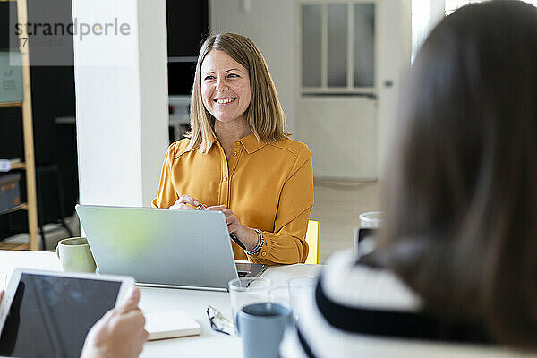 Lächelnde Geschäftsfrau mit Laptop sitzt im Büro