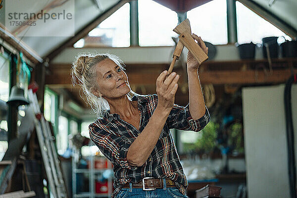 Frau hält Holzwerkzeug am Gartenschuppen