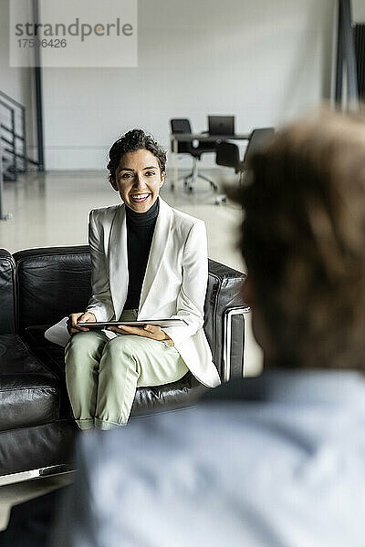 Lächelnde Geschäftsfrau mit Tablet-PC diskutiert mit Kollege in der Lobby