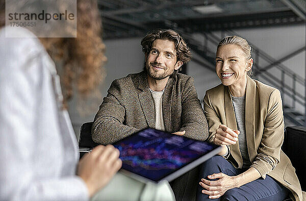 Glückliche Geschäftsfrau mit Geschäftsmann  der einen Kollegen ansieht  der an einem Tablet-PC arbeitet