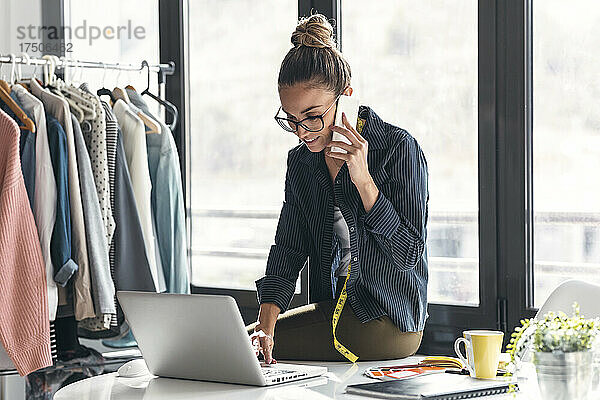 Lächelnde Geschäftsfrau benutzt Laptop und telefoniert im Büro