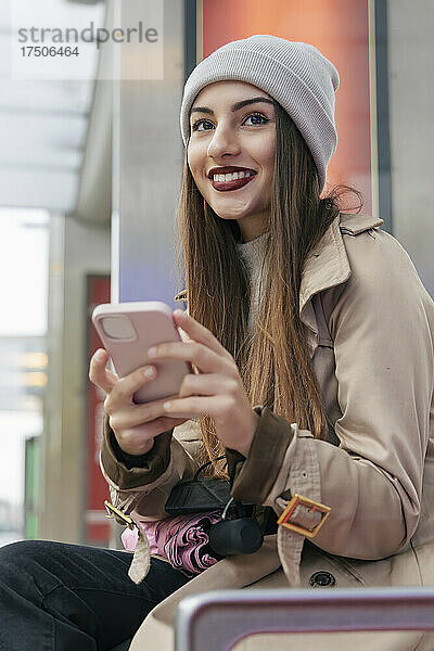 Nachdenkliche Frau in warmer Kleidung hält Smartphone in der Hand
