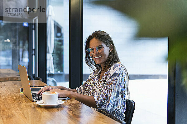 Lächelnde Geschäftsfrau mit Laptop sitzt im Café