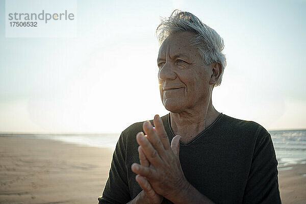 Lächelnder älterer Mann mit gefalteten Händen am Strand