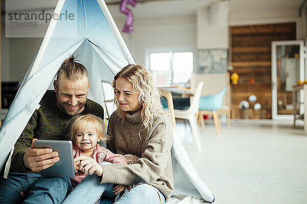 Glückliche Familie sitzt im Zelt und nutzt zu Hause ein digitales Tablet