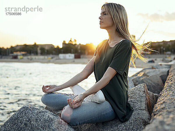 Blonde Frau meditiert auf einem Felsen am Strand von Bogatell  Barcelona  ??Katalonien  Spanien