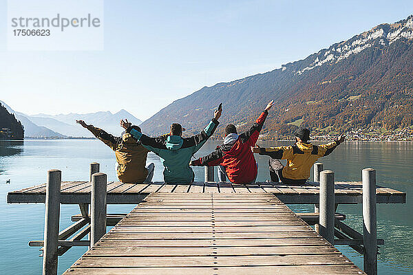 Sorglose Freunde sitzen mit erhobenen Armen auf dem Pier in Interlaken  Schweiz