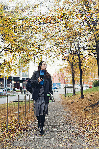 Geschäftsfrau mit Smartphone läuft im Herbst auf Fußweg