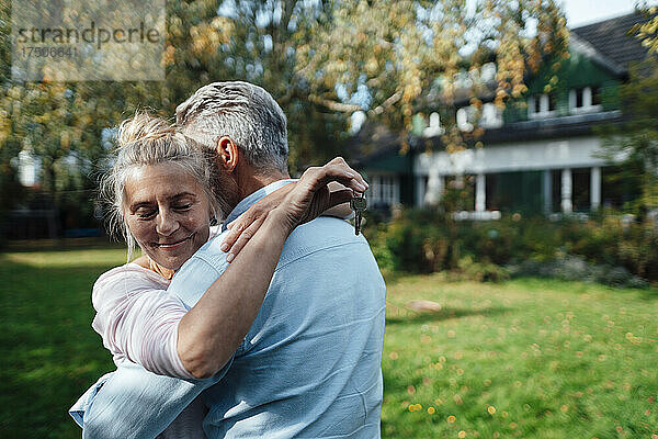 Lächelnde Frau hält Hausschlüssel in der Hand und umarmt Mann im Hinterhof
