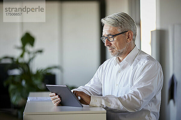 Reifer Geschäftsmann arbeitet an einem Tablet-PC am Schalter im Büro