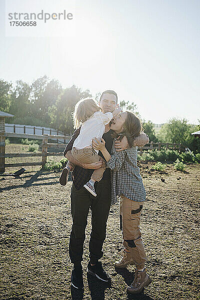 Mann trägt Mädchen und umarmt Frau auf dem Bauernhof