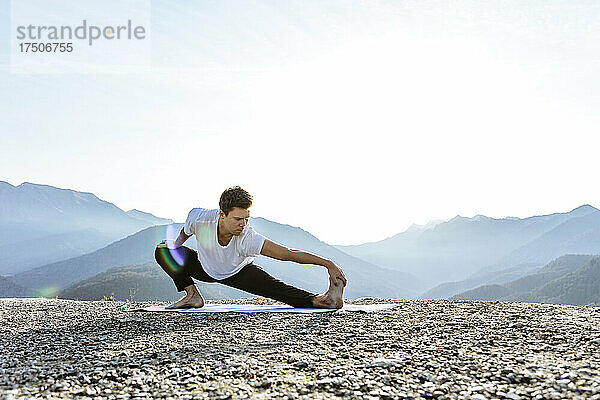 Flexibler Mann  der Skandasana mit Blick auf die Berge praktiziert