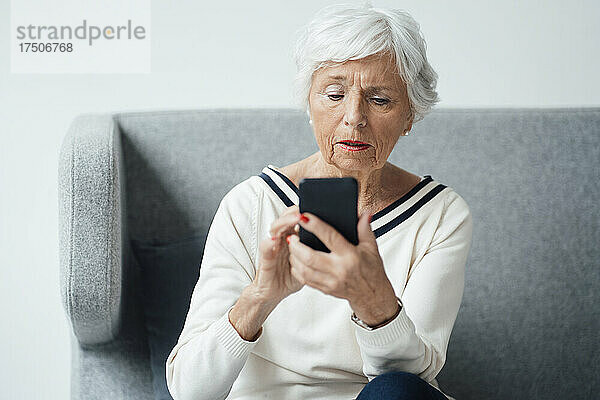 Ältere Frau benutzt Mobiltelefon auf Sofa