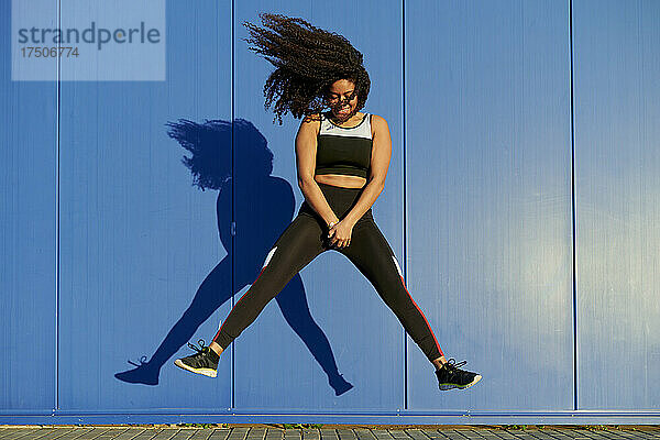 Sportlerin springt breitbeinig vor blauer Wand