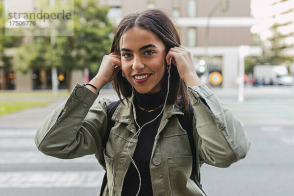 Lächelnde Frau mit In-Ear-Kopfhörern unterwegs