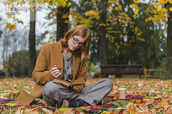 Frau mit Stift liest Buch im Herbstpark