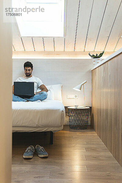 Geschäftsmann benutzt Laptop auf Bett im Dachboden zu Hause