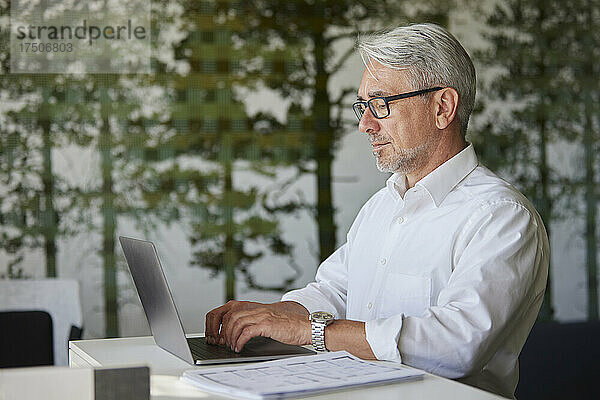 Geschäftsmann mit Brille arbeitet im Büro am Laptop