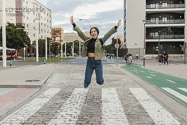 Sorglose Frau mit ausgestreckten Armen springt auf der Straße