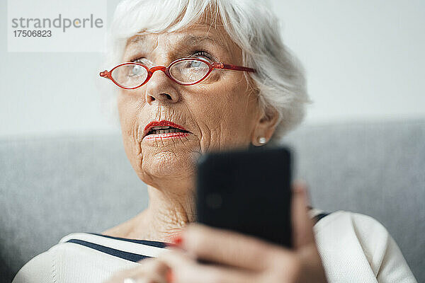 Frau mit Brille hält Mobiltelefon zu Hause
