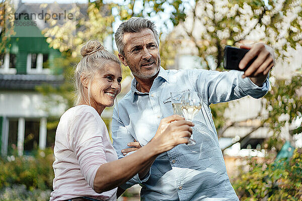 Lächelnder Mann macht Selfie mit Frau per Handy im Hinterhof