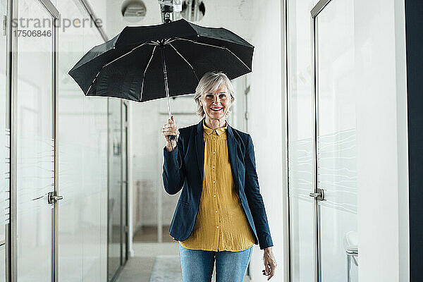 Lächelnde Geschäftsfrau mit Regenschirm im Büroflur