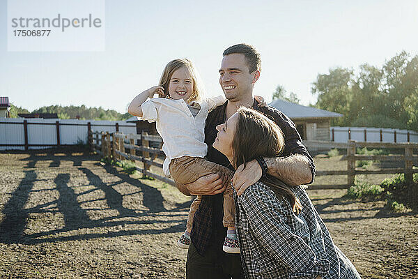Lächelnder Mann und Frau mit Tochter stehen auf dem Bauernhof