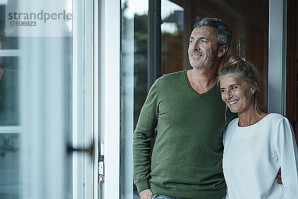 Lächelndes Paar zu Hause  das aus dem Fenster schaut