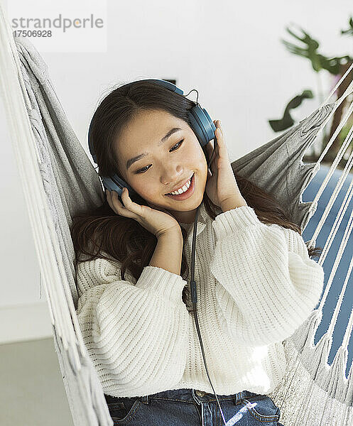 Junge Frau hört zu Hause in der Hängematte Musik über Kopfhörer