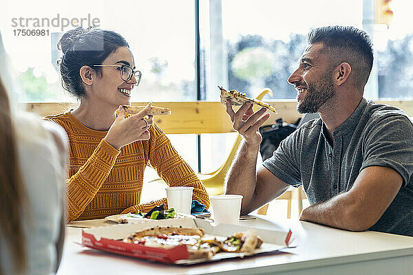 Lächelnder Geschäftsmann isst Pizza mit Geschäftsfrau in der Mittagspause