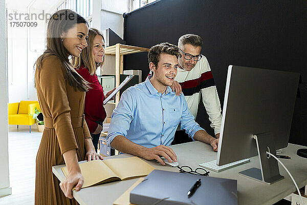 Junger Geschäftsmann nutzt Desktop-PC mit Kollegen  die im Büro am Schreibtisch stehen