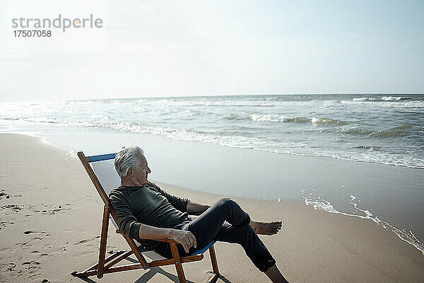 Älterer Mann sitzt auf einem Stuhl am Strand