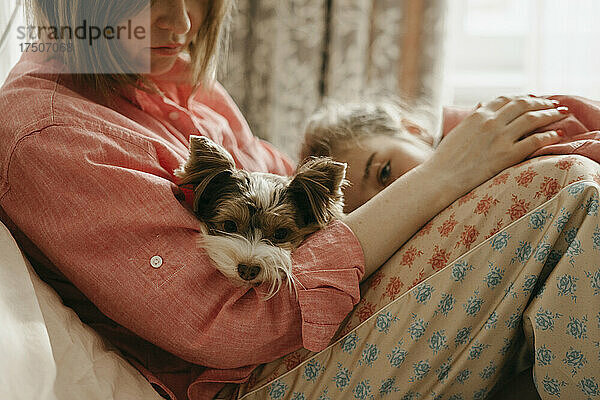 Frau mit Hund und Tochter sitzt im Schlafzimmer
