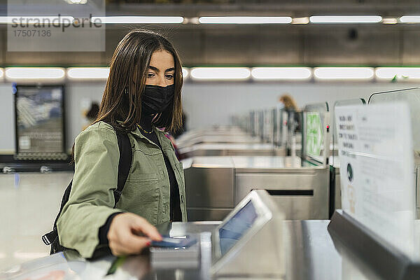 Frau mit Gesichtsmaske bezahlt an Sicherheitsschranke in der U-Bahn