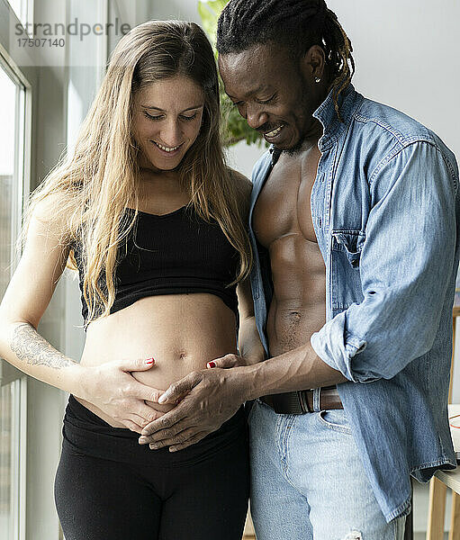Glückliches Paar erwartet ein Baby und schaut zu Hause auf den Bauch einer schwangeren Frau