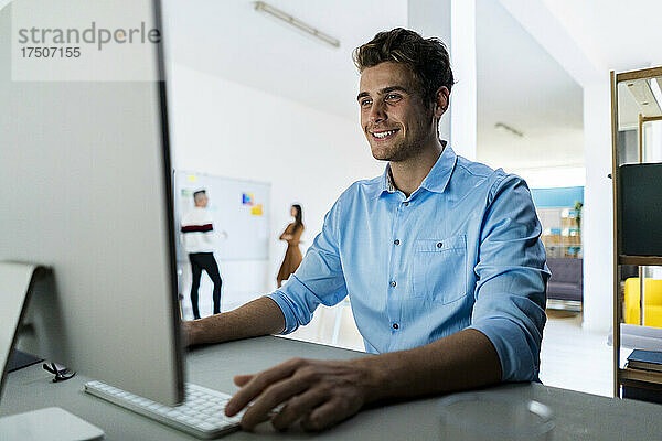 Lächelnder Geschäftsmann  der im Büro am Desktop-PC arbeitet