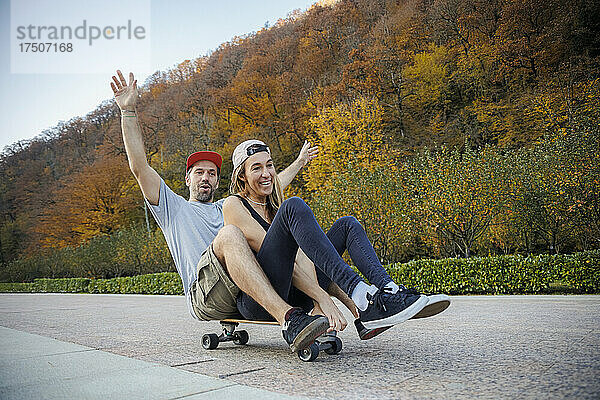 Verspieltes Paar fährt gemeinsam Skateboard auf Fußweg