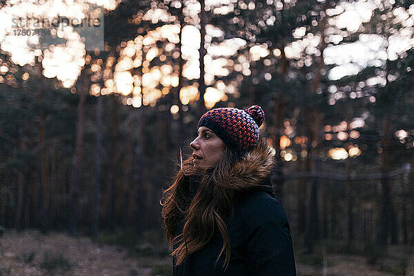 Frau mit Strickmütze im Wald bei Sonnenuntergang