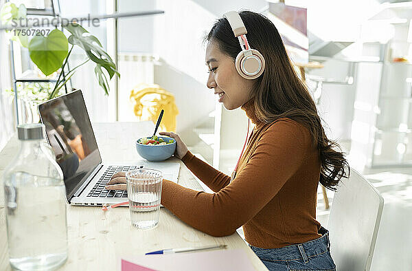 Junge Geschäftsfrau mit Kopfhörern nutzt Laptop im Heimbüro