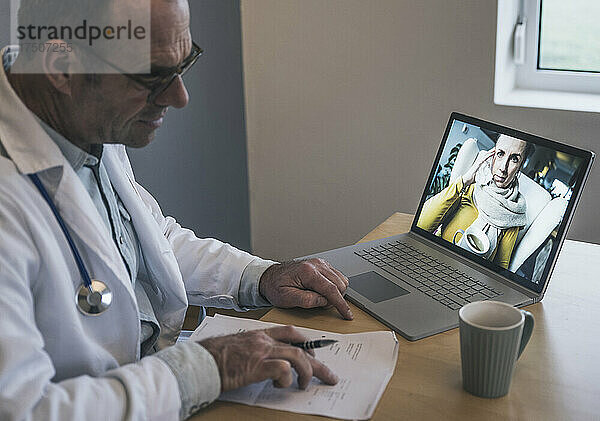 Arzt bespricht medizinische Berichte mit Patient per Videoanruf über Laptop in der Klinik
