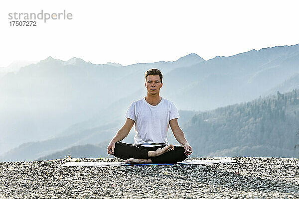 Mann meditiert im Lotussitz mit Blick auf die Berge